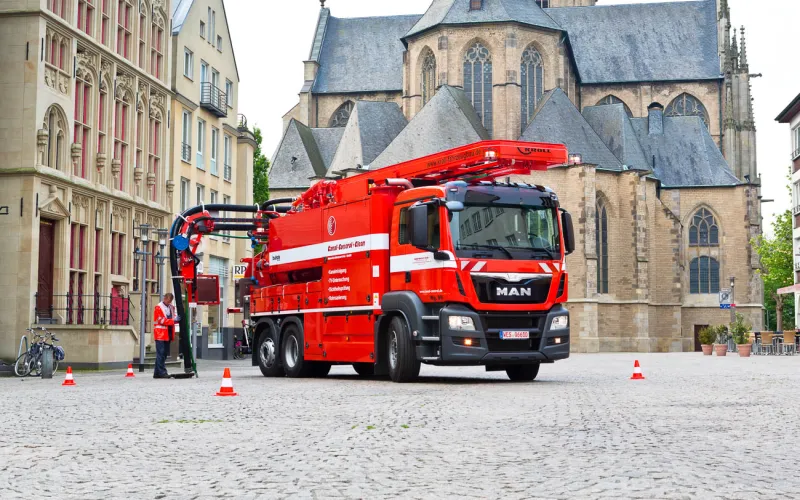 Rotes KROLL WRS 2 auf MAN-Fahrgestell im Einsatz auf einem Altstadtplatz vor einer Kirche, ein Arbeiter am Schacht
