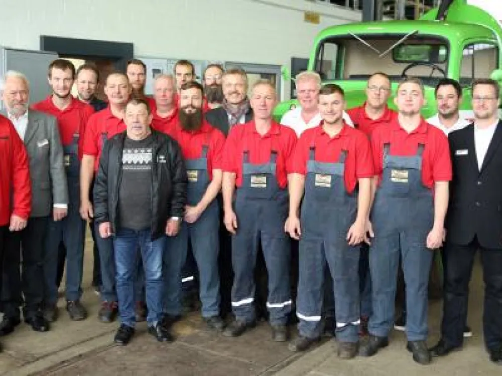Das Team des KROLL Truck & Service Centers in der Werkstatthalle, im Hintergrund ein grünes Saugfahrzeug