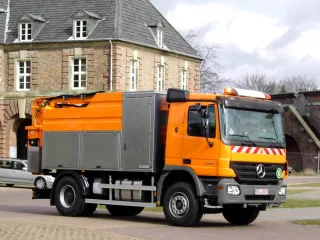 Orangefarbenes HD-Spülfahrzeug auf Mercedes-Fahrgestell mit Edelstahl-Geräteschränken vor einem historischen Backsteingebäude