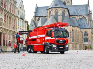 Rotes KROLL WRS 2 auf MAN-Fahrgestell im Einsatz auf einem Altstadtplatz vor einer Kirche, ein Arbeiter am Schacht
