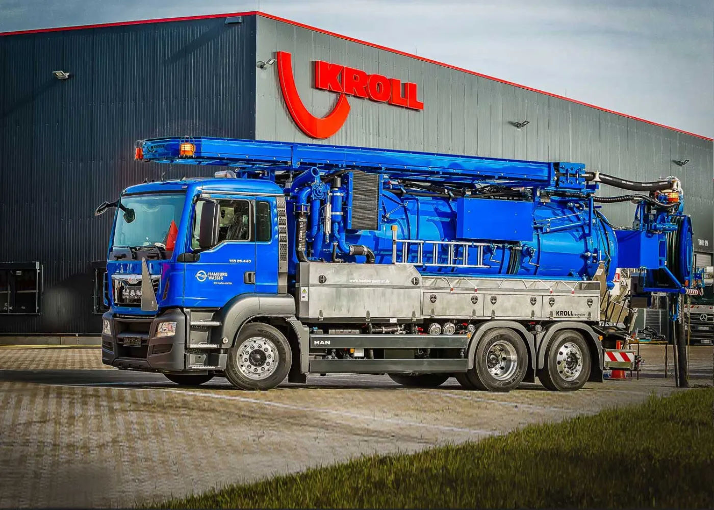 Blaues KROLL-Saug-Spülfahrzeug mit langem Ausleger vor der Werkshalle mit KROLL-Schriftzug
